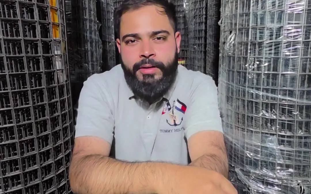 Shop owner seated beside welded mesh rolls